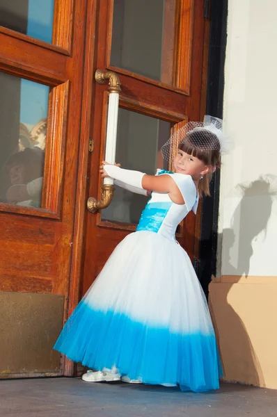 Colegiala en vestido elegante azul y blanco cerca de la puerta de madera —  Fotos de Stock