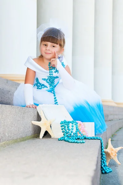 休日の白と青のドレスでかわいい女の子が列の近くの階段に座っています。 — ストック写真