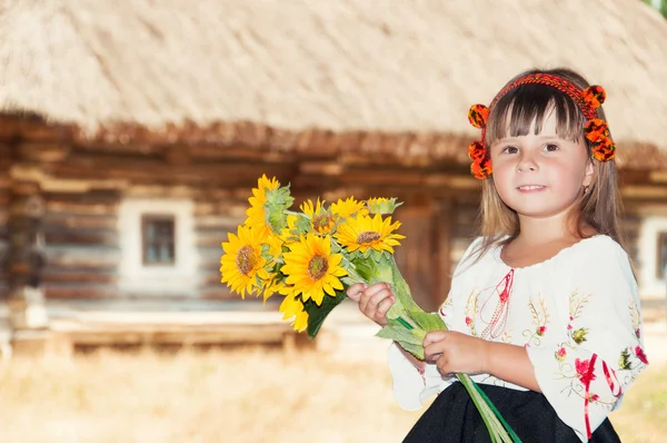 Дівчина з соняшниками і гуцульським вінком в селі зі старим дерев'яним будинком — стокове фото