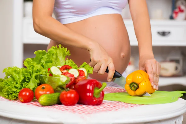 Närbild av en gravid mage. Gravid kvinna i köket förbereder en grönsakssallad. — Stockfoto