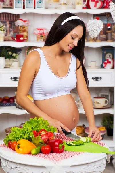 Pregnant woman in the kitchen preparing a vegetable salad. Healthy nutritious. Last months of pregnancy. Stock Photo