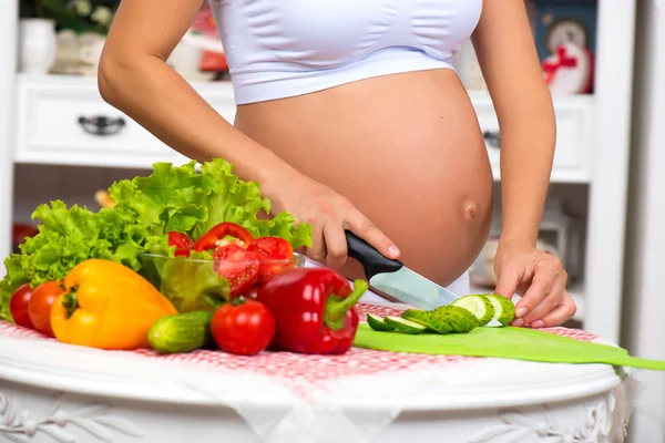 Close-up of a pregnant belly. Pregnant woman in the kitchen preparing a vegetable salad. Royalty Free Stock Images