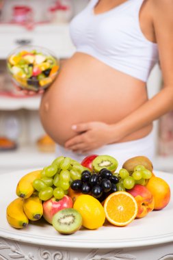 Taze meyve ve salata tabağı ile hamile bir karın close-up. Sağlıklı gebelik, diyet ve vitaminler