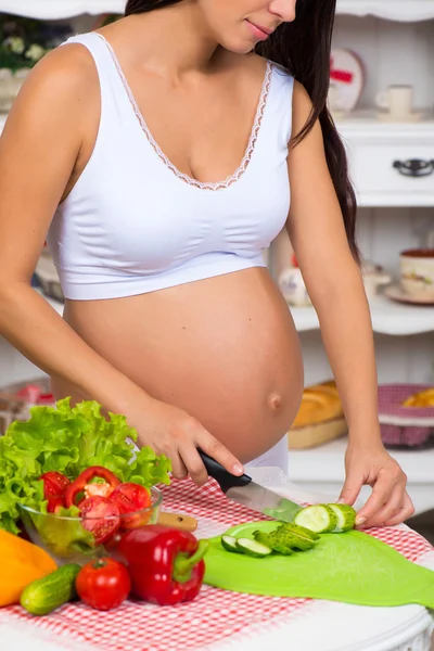 Primer plano. Mujer embarazada en la cocina corta diferentes verduras en ensalada de primavera . — Foto de Stock