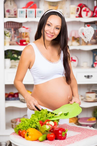 Nutrizione sana e gravidanza. Giovane donna incinta sorridente taglia verdure su insalata — Foto Stock