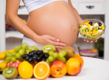 Taze meyve ve salata tabağı ile hamile karnına close-up. Sağlıklı gebelik, diyet ve vitaminler