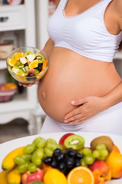 Taze meyve ve salata tabağı ile hamile bir karın close-up. Sağlıklı gebelik, diyet ve vitaminler
