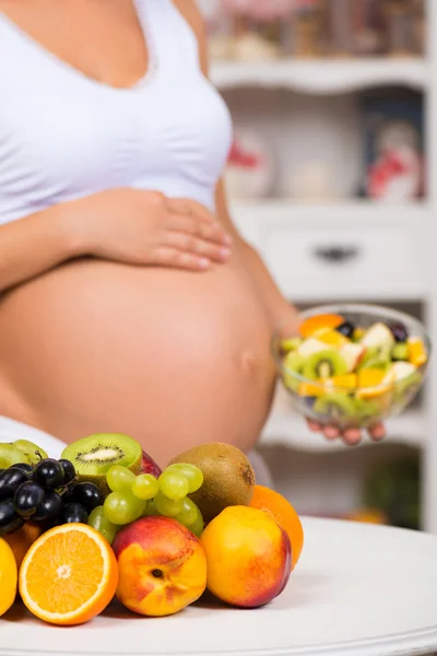 Nahaufnahme eines schwangeren Bauches mit frischem Obst und einem Teller Salat. gesunde Schwangerschaft, Ernährung und Vitamine — Stockfoto