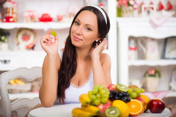 Beautiful brunette girl sitting at the kitchen table with a plate of fresh fruit. Diet, healthy food and vitamins — Stock Photo, Image