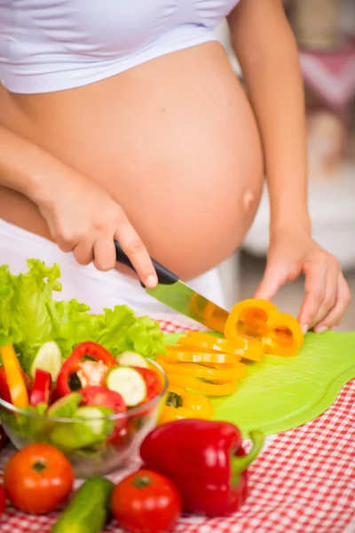 Närbild av en gravid mage. Gravid kvinna i köket förbereder en grönsakssallad. — Stockfoto