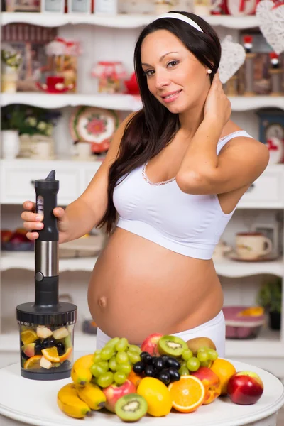 Hamile kadın kesme meyve mutfak blender ile gülümseyen — Stok fotoğraf