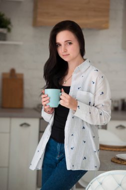Genç bir kız öğrenci sabah mutfakta elinde bir fincan kahve ya da çayla durur. Günlük kıyafet giymiş kadın kot pantolon ve gömlek.