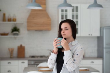 Genç bir kız öğrenci sabah mutfakta elinde bir fincan kahve ya da çayla durur. Günlük kıyafet giymiş kadın kot pantolon ve gömlek.