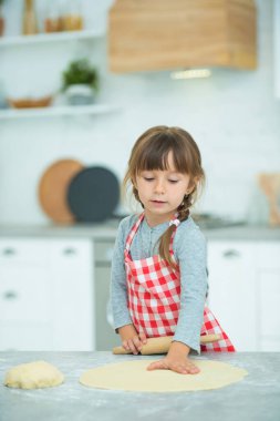 Ekose önlüklü, saçları örgülü, pizza hamurunu kendi yoğuran tatlı bir kız. Çocuklar için aşçılık dersleri.