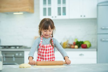 Ekose önlüklü, saçları örgülü, pizza hamurunu kendi yoğuran tatlı bir kız. Çocuklar için aşçılık dersleri.