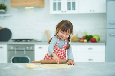 Ekose önlüklü, saçları örgülü, pizza hamurunu kendi yoğuran tatlı bir kız. Çocuklar için aşçılık dersleri.