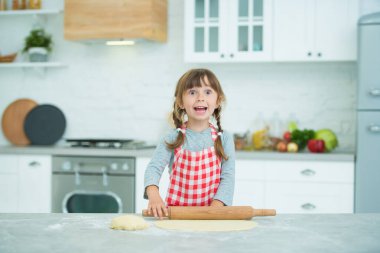 Ekose önlüklü, saçları örgülü, pizza hamurunu kendi yoğuran tatlı bir kız. Çocuklar için aşçılık dersleri.