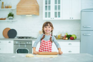 Ekose önlüklü, saçları örgülü, pizza hamurunu kendi yoğuran tatlı bir kız. Çocuklar için aşçılık dersleri.