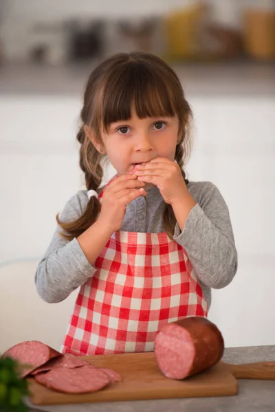 Cute Little Girl Pigtails Checkered Culinary Apron Eating Sausage Kitchen — Stock Photo, Image