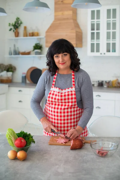 Kareli önlüklü kadın pizza malzemesi için mutfakta sosis kesiyor..