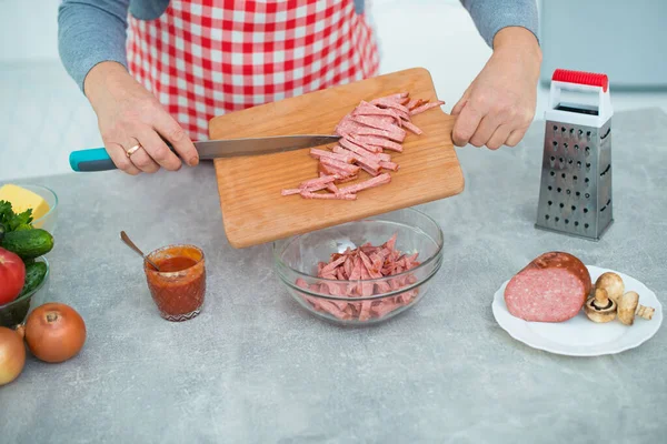Kareli önlüklü kadın pizza malzemesi için mutfakta sosis kesiyor..