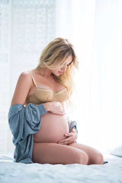 Beautiful pregnant blonde woman sitting at home in bed. Femininity and beauty. The concept of a happy and healthy pregnancy.