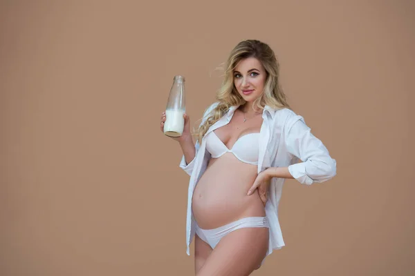 셔츠와 속옷을 아름다운 임신부가 베이지 배경에 술병을 — 스톡 사진