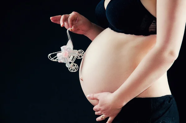 Zwangere buik close-up op zwarte achtergrond. speelgoed pram als symbool van verwachtingen van baby — Stockfoto