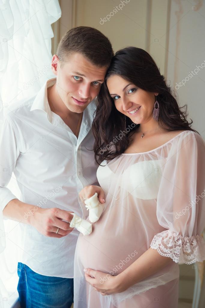 Gentle beautiful pregnant couple near tulle curtains