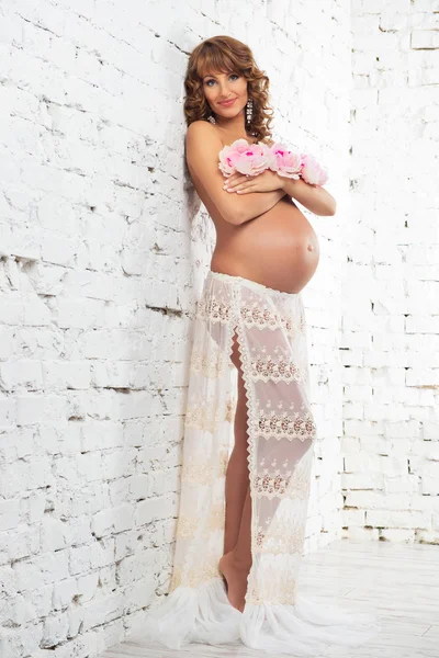 Beautiful half-naked pregnant girl near a white brick wall Stock Photo