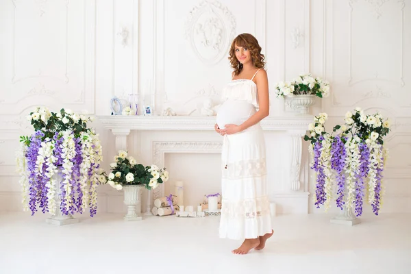 Mooie zwangere vrouw in lichte kleding in het interieur in de buurt van de open haard — Stockfoto
