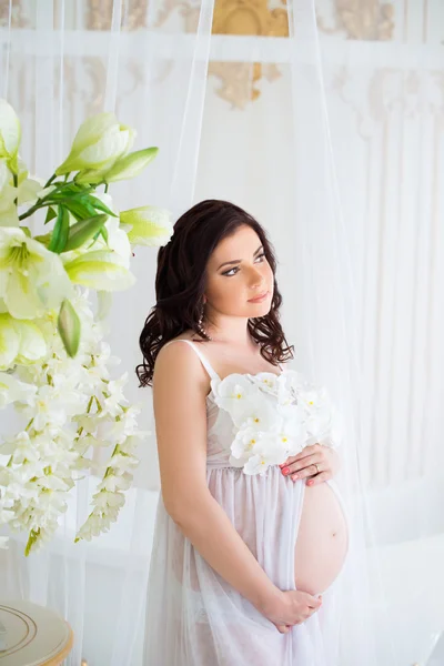 Sehr sanfte schwangere Mädchen im Inneren mit Blumen und Tüll Vorhänge — Stockfoto