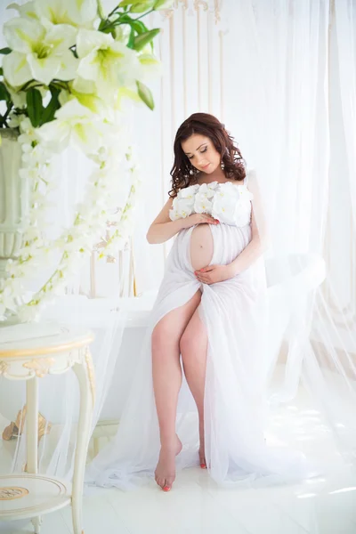 Brunette pregnant girl in interior bath with flowers and tulle curtains