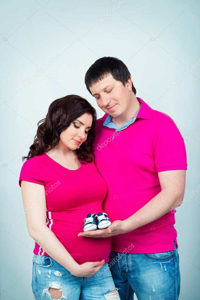 Young beautiful pregnant couple in crimson shirt with baby booties in hands