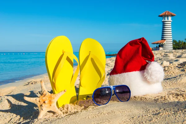 Weihnachten und Neujahr Urlaub am Meer. Weihnachtsmütze, Sandalen, Sonnenbrille am Sandstrand — Stockfoto