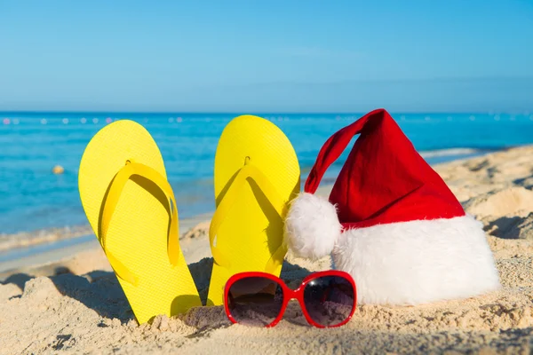 Christmas vacation at sea. Happy  New Year holidays. Santa hat, sandals, sunglasses on sandy beach — Stock Photo, Image