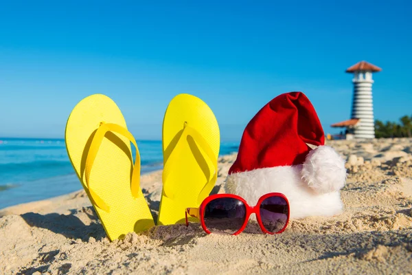 Christmas vacation at sea. Happy  New Year holidays. Santa hat, sandals, sunglasses on sandy beach — Stock Photo, Image