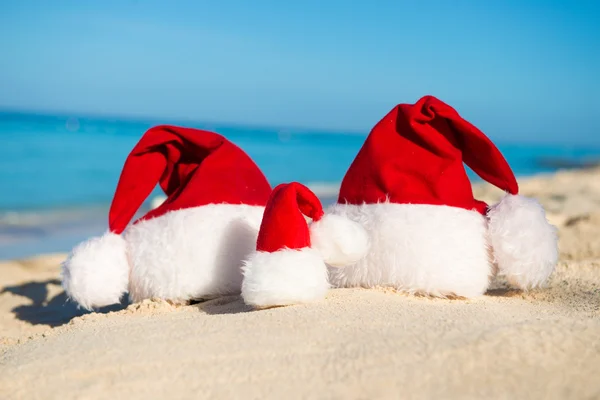 Santa hats on sandy beach  - concept of New Year family holiday with the children on the sea. — ストック写真