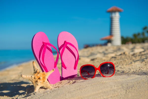 Accesorios marinos para mujer: sandalias, gafas de sol y estrellas de mar en la playa de arena tropical sobre el fondo del faro — Foto de Stock