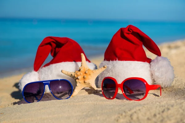 Christmas holidays and Romantic New Year at Sea. Santa hats and sunglasses on sandy beach — ストック写真
