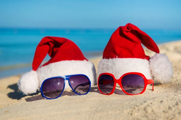 Christmas holidays and Romantic New Year at Sea. Santa hats and sunglasses on sandy beach — 스톡 사진