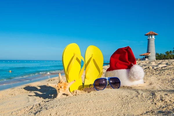 Christmas and New Year holidays at the sea. Santa hat, sandals, sunglasses on sandy beach — Zdjęcie stockowe