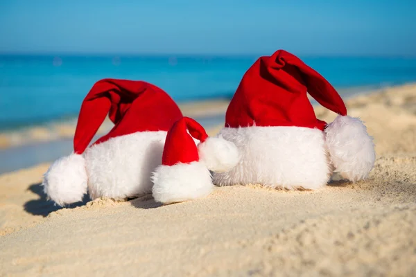 Santa hats on sandy beach  - concept of New Year family holiday with the children on the sea. — Stock Fotó