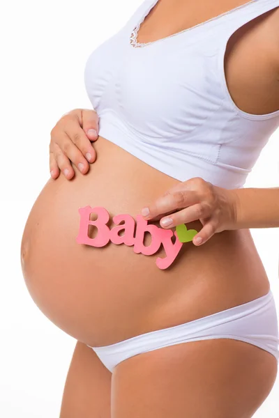Pink label "Baby" a kezében terhes nő. Az újszülött lánya. Terhes hasa közelről, fehér alapon. — Stock Fotó