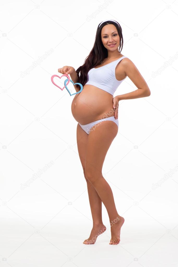 Pregnant girl in full growth on white background isolated. Expectant mother holding  plate of blue and pink hearts.