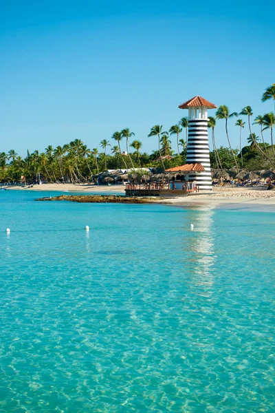 Striped lighthouse on sandy shore with palm trees. Clear water of the Caribbean sea. — Stock Photo, Image