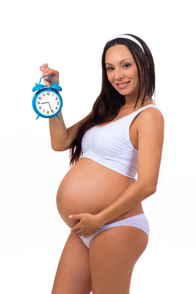 Χαμογελώντας έγκυος γυναίκα εκμετάλλευση ξυπνητήρι. Κάθετη φωτογραφία σε άσπρο φόντο. — Φωτογραφία Αρχείου