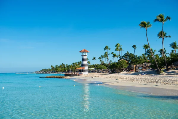 Átlátszó tenger víz és a tiszta ég. Világítótorony egy homokos trópusi szigeten, pálmafákkal. — Stock Fotó