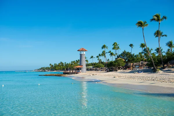 Transparent sea water and clear sky. Lighthouse on a sandy tropical island with palm trees. — Stock Photo, Image