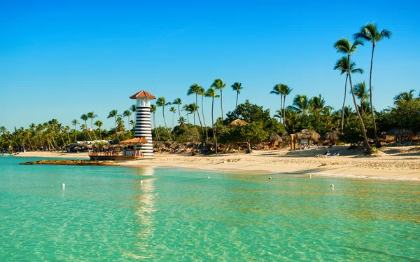 Eau de mer transparente et ciel clair. Phare sur une île tropicale sablonneuse avec palmiers . — Photo